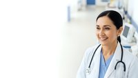 Smiling female doctor with stethoscope in white coat at modern medical clinic. Professional healthcare worker portrait for medical websites and marketing.