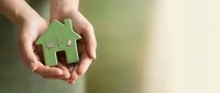 Hands gently holding green paper house cutout symbolizing home protection, real estate investment, mortgage insurance and property care concept.
