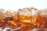 Ice cubes splashing in amber liquid creating dynamic waves and ripples with golden highlights, macro photography showing refreshing beverage details.