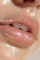 Close-up of glossy nude lips with sparkly glitter makeup effect, showing white teeth. Macro beauty shot highlighting moisturized skin and glamorous cosmetic application.