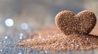 Glittering rose gold heart shape on sparkly surface with soft bokeh background creates romantic Valentine's Day or wedding celebration atmosphere.