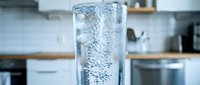 Fresh sparkling water with bubbles in clear glass on modern kitchen counter. Refreshing drink for healthy lifestyle and hydration concept.
