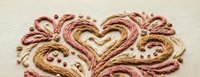 Embroidered heart design with decorative swirls in pink and gold thread on cream fabric. Romantic needlework pattern for crafting and textile projects.