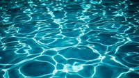 Crystal clear turquoise swimming pool water with sunlight creating rippling patterns and caustic reflections on the surface for summer vacation concepts.