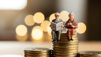 Senior couple figurines sitting on stacks of golden coins representing retirement savings and financial planning for elderly lifestyle security.