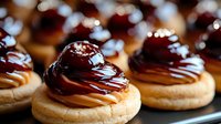 Delicate pastries with chocolate and caramel drizzle on golden shortbread cookies arranged in rows, creating an appetizing dessert display for food photography and menus.