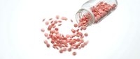 Pink capsules spilling from glass bottle in dynamic motion on white background for pharmaceutical and healthcare design concepts.