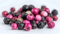 Fresh pink and black peppercorns scattered on white surface, showcasing vibrant colors and textures for culinary and food photography use.