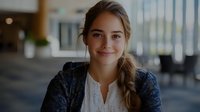 Young professional woman smiling confidently in modern office environment with natural lighting and contemporary workspace background.
