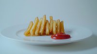 Golden crispy french fries served on white ceramic plate with bright red ketchup dipping sauce, minimalist food photography against neutral background.