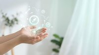 Hands presenting glowing energy icons in modern bright interior space with plants and natural light for wellness and sustainability concepts.