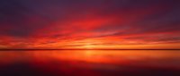 Dramatic red and orange sunset over calm water with vibrant sky gradient, suitable for backgrounds, nature themes, and atmospheric design projects.