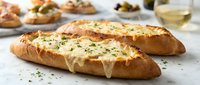 Toasted baguette slices topped with melted cheese and fresh herbs on white surface. Gourmet appetizer bread with golden cheese perfect for restaurant menus.