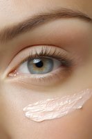 Close-up of light blue eye with natural eyebrow and moisturizing cream streak on smooth skin, showcasing skincare and cosmetic application technique.