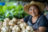 Smiling Hispanic farmer in straw hat displaying fresh harvested Jerusalem artichokes at local market. Natural lighting highlights organic produce and authentic farm-to-table experience.