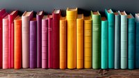 Colorful hardcover books arranged in rainbow order standing in row on wooden shelf, spines showing gradient from red through yellow to turquoise colors.