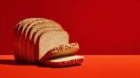Freshly sliced whole wheat bread loaf on vibrant red background, creating striking contrast for food photography or bakery advertising.