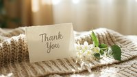 Handwritten thank you card with white flowers on cozy knit fabric in warm soft light, evoking gratitude and appreciation.