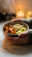 Hands holding warm bowl with quinoa, roasted sweet potato and lime slice, steam rising, candlelit ambiance, cozy wellness and healthy eating concept for lifestyle and nutrition content.