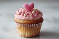 Pink frosted cupcake topped with heart decoration and colorful sprinkles for Valentine's Day celebration, romantic dessert bakery treat.