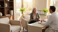 Professional blonde businesswoman consulting with male client in modern bright office interior with natural lighting and plants.