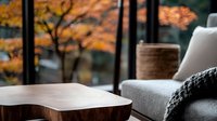 Cozy autumn interior with wooden coffee table and gray sofa near window with fall foliage view. Knitted throw blanket creates warm atmosphere.