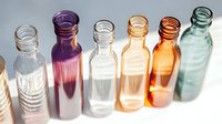Colorful glass bottles in row on white background with sunlight creating shadows and reflections. Minimalist composition for wellness, aromatherapy and spa design.