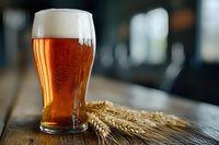 Fresh cold craft beer glass with foam head and wheat ears on rustic wooden table in pub setting, selective focus on amber liquid.