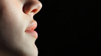 Close-up profile view of young caucasian woman's face showing soft pink lips and nose against dark background, dramatic side lighting creates sensual mood.
