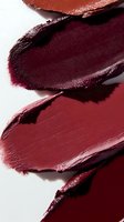 Macro shot of burgundy and wine-colored lipstick smears showing rich texture and creamy consistency against white background, showcasing cosmetic product swatches.