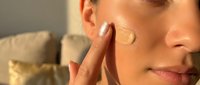 Young woman applying facial cream or foundation with finger on cheek in natural lighting for skincare routine and beauty care concept.