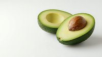 Fresh ripe avocado cut in half showing creamy green flesh and brown pit on clean white background isolated for healthy food design projects.