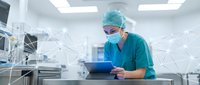 Male surgeon in green scrubs and surgical mask using digital tablet in modern operating room with network connectivity overlay for telemedicine applications.