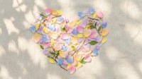 Heart shape made of colorful pastel flower petals and green twigs on linen fabric with soft natural shadows.