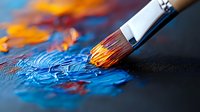 Paintbrush with orange and blue oil paint on canvas, macro shot showing detailed bristles and textured paint strokes in vibrant contrasting colors against dark background.