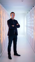 Confident Caucasian male IT professional standing with crossed arms in modern server room data center corridor for technology business concepts.