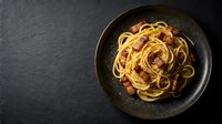 Cooked spaghetti pasta with garlic and oil served in dark bowl on slate surface, overhead view for food photography and culinary content.