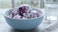 Purple ice cream scoops in light blue bowl on table with glass of water, suitable for food, dessert, and culinary design projects.
