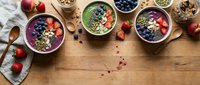 Colorful smoothie bowls topped with fresh berries, seeds and nuts arranged on wooden table for healthy breakfast meal preparation and nutrition.