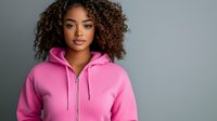 Young woman with curly hair wearing bright pink zip-up hoodie against gray background, looking confidently at camera.