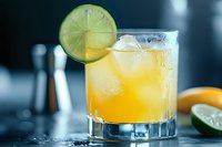 Refreshing citrus cocktail with lime garnish and ice cubes in glass tumbler on dark background. Cold alcoholic beverage for summer parties and bar service.
