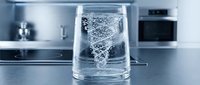 Clear glass filled with sparkling water showing effervescent bubbles rising to surface in modern kitchen setting for healthy hydration lifestyle.