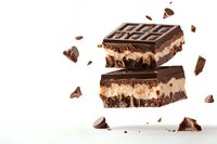 Layered chocolate dessert bars with cream filling and scattered chocolate pieces floating on white background, isolated food photography for confectionery advertising.