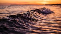 Ocean waves at golden sunset with warm orange sky reflecting on water surface creating peaceful seascape moment for relaxation and meditation backgrounds.