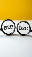 Pair of eyeglasses with B2B and B2C text on lenses against yellow and white background, representing business models and marketing strategies for corporate and consumer sales.
