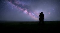 Silhouette of a romantic couple embracing under a breathtaking Milky Way galaxy, standing on a dark field beneath a vivid starry night sky.