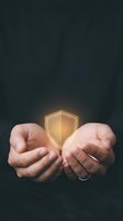 Hands holding glowing golden shield symbol against dark background, representing data protection, cybersecurity, insurance, and digital safety for business concepts.