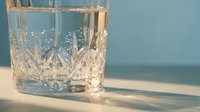 Crystal cut glass tumbler with intricate diamond pattern casting elegant shadows on wooden surface in soft natural light for luxury beverage presentation.