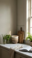 Minimalist kitchen counter with marble surface, stacked ceramic bowls, wooden cutting boards, fresh herbs, and soft natural window light.