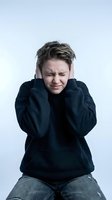Young Caucasian man in black hoodie covering ears with hands, expressing pain or stress from loud noise, isolated on white background for health concepts.